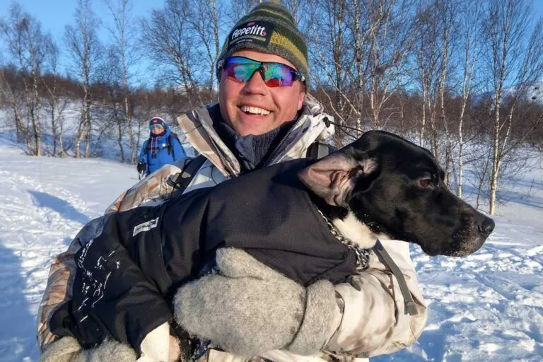 Hundetrener og Appetitt ambassadør Bertil Nyheim trener hund til jakt, her ute i vintersolen med hund i armene sine mens han smiler glad.