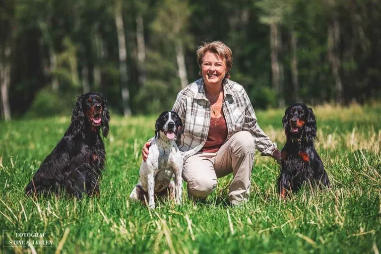 Eier av Sando Hundesenter Hanne Fevik her portrettert sammen med tre hunder utendørs i sommergrønne omgivelser.