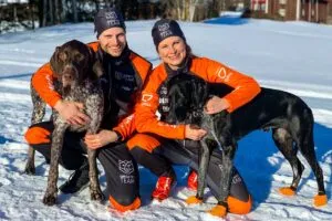 Yvette og Yngve Hoel poserer sittende i snøen sammen med hver sin hund.