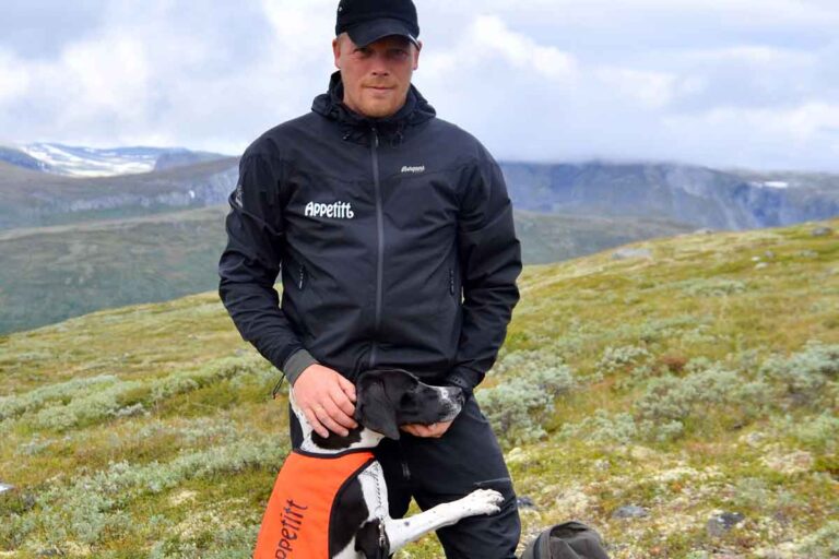 Appetitt ambassadør Stian Henriksen på tur på fjellet med en av sine hunder. Stian har Appetitt-logo på sin jakke, og hunden har oransje vest med Appetitt-logo.